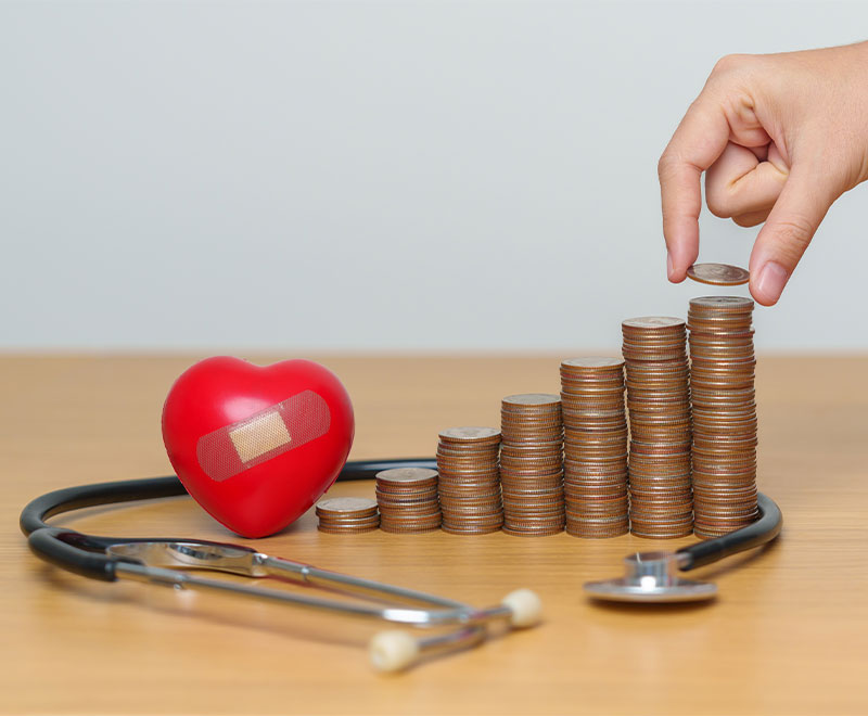 Photo of stethoscope, piles of quarters, a heart with a bandaid and a human hand