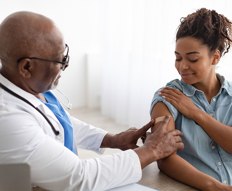 Photo of doctor putting a bandaid on a patient after administering a vaccine