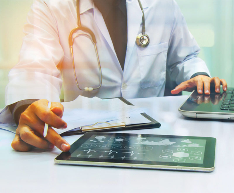 Photo of a healthcare worker using an iPad and laptop