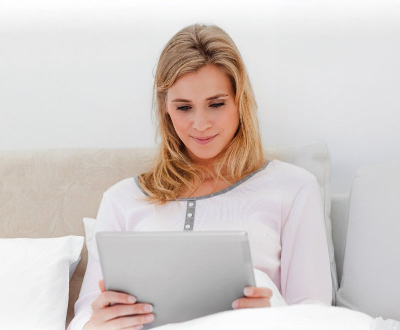 Photo of a young blonde woman in bed, looking at an iPad