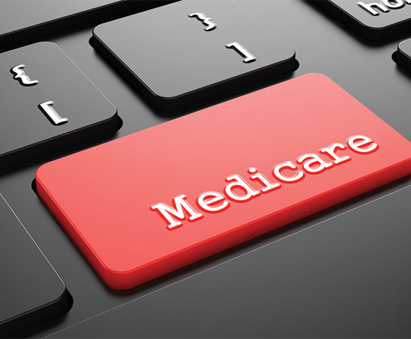 Close up photo of a computer keyboard, honing in on an "enter" button that is red and says "Medicare."