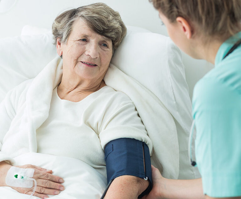 Photo of an elderly female patient in a hospital bed with a blood pressure cuff