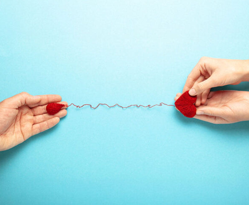 Hands holding a heart and a blood drop connected by a red string