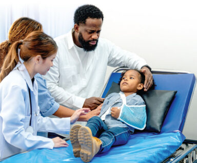 Parents comfort a child lying on a medical table.