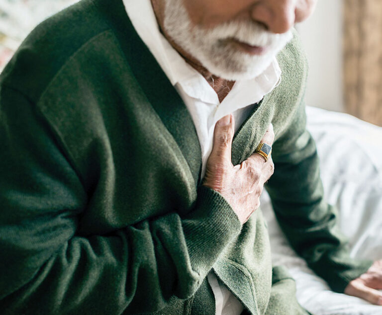 Man wearing a green button-up sweater clutching at his chest.