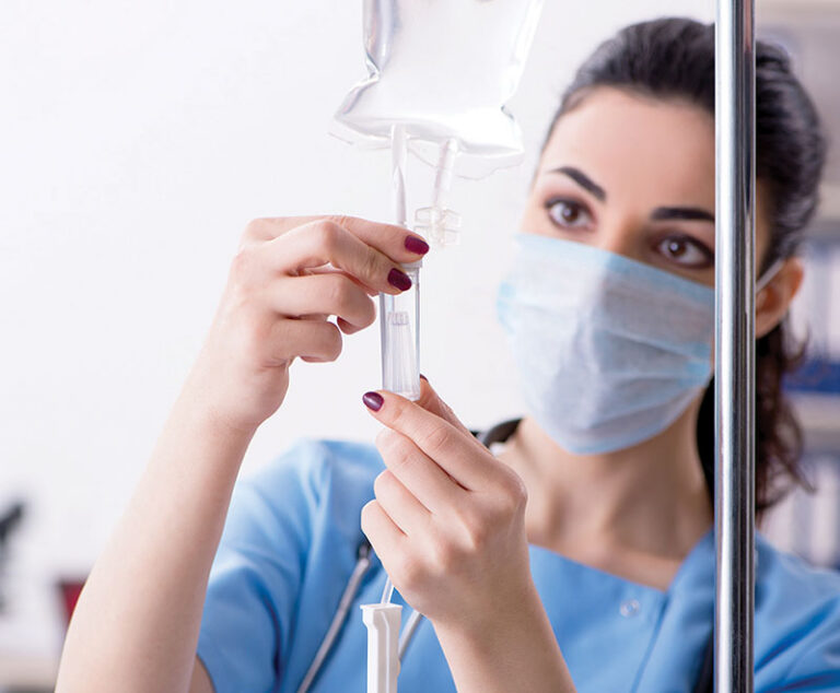 Nurse wearing a medical mask preparing an IV solution.