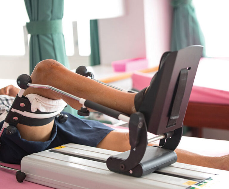Person lying down with foot resting on a physical therapy machine for knee surgery recovery.