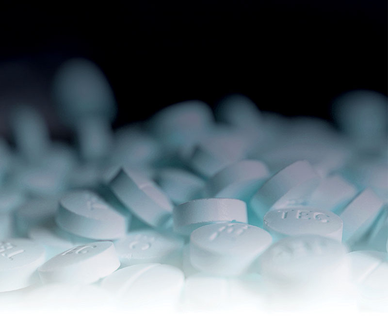 Many white pills against a black background.